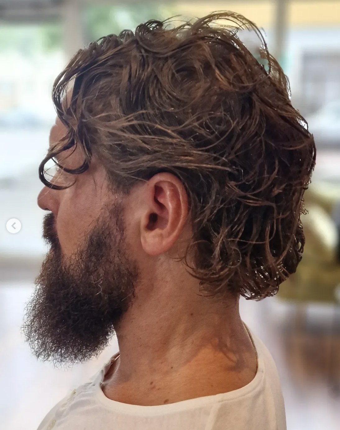 Herrfrisyr med naturliga lockar och trimmat skägg