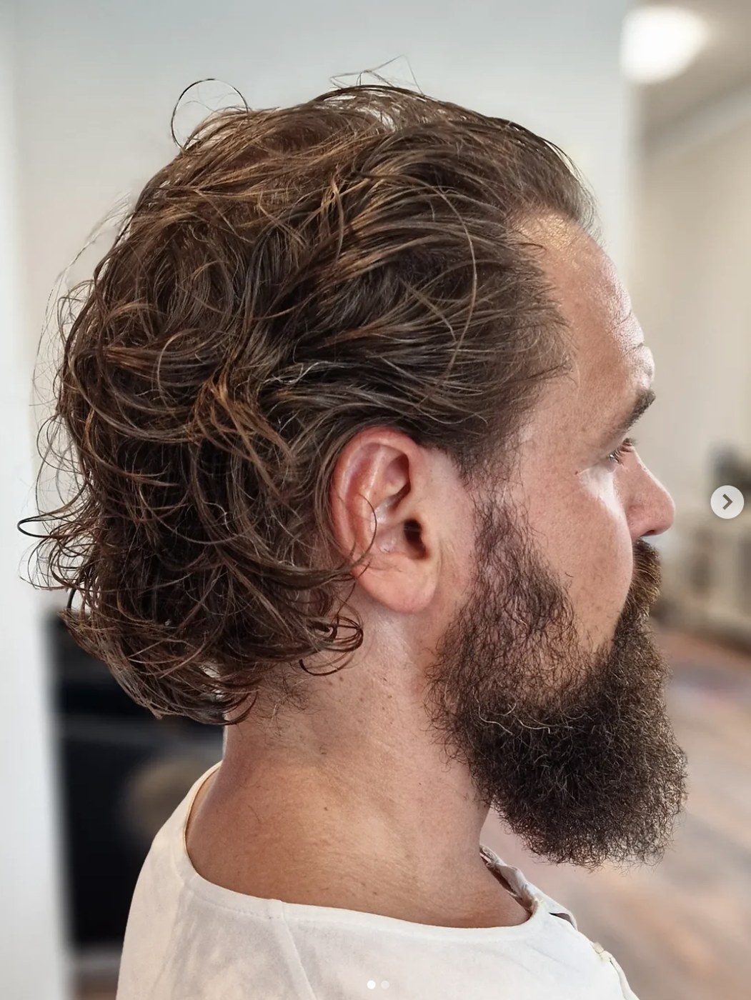 Herrklippning med vågigt lockigt hår och välvårdat skägg